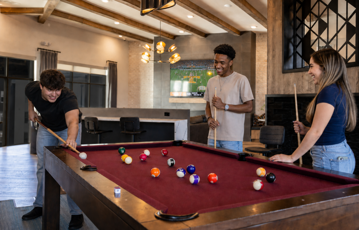 Three friends play pool in a clubhouse while a football game plays on TV