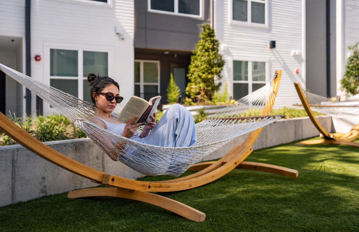 Woman wearing sunglasses reads in a hammock in a sunny apartment courtyard